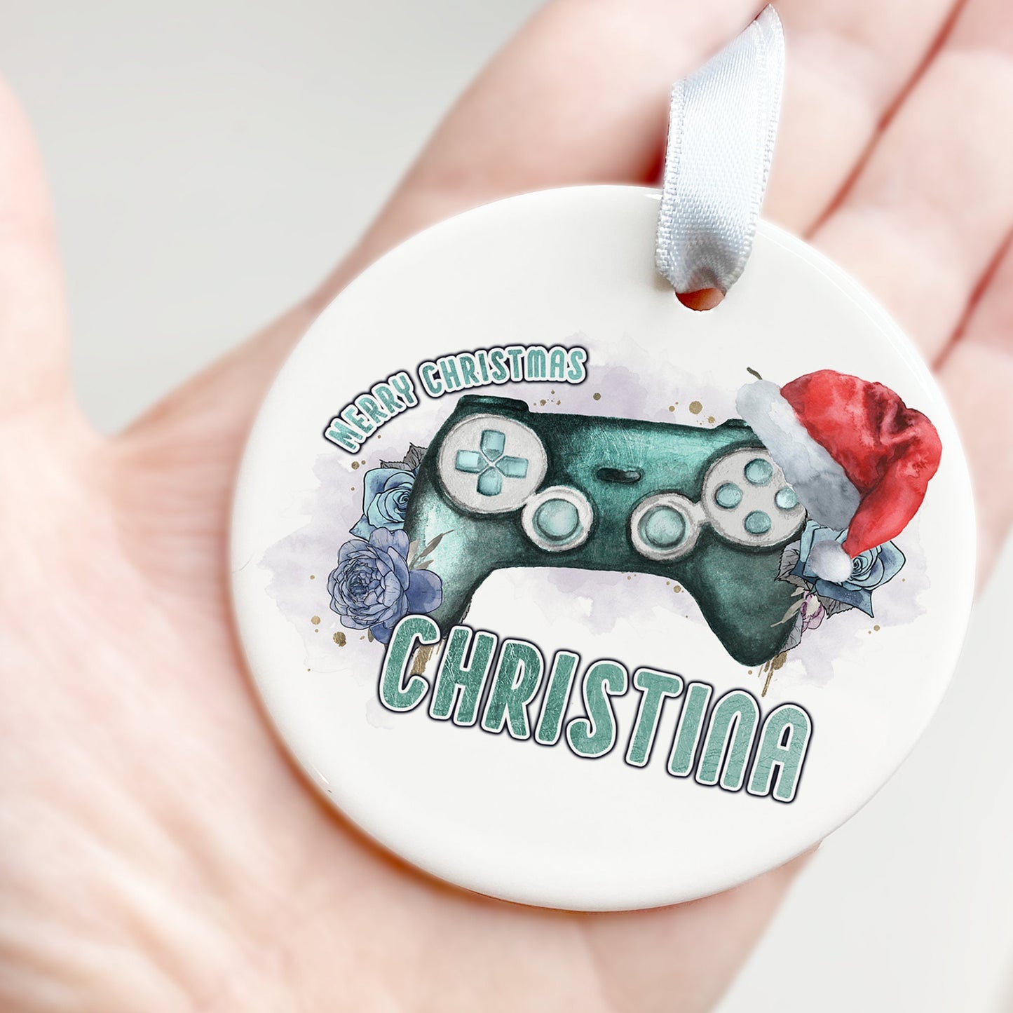 White Ceramic personalised Christmas bauble in gift box. Festive teal coloured gaming Controller with teal florals and christmas hat and matching teal text in the words Merry Christmas Name.