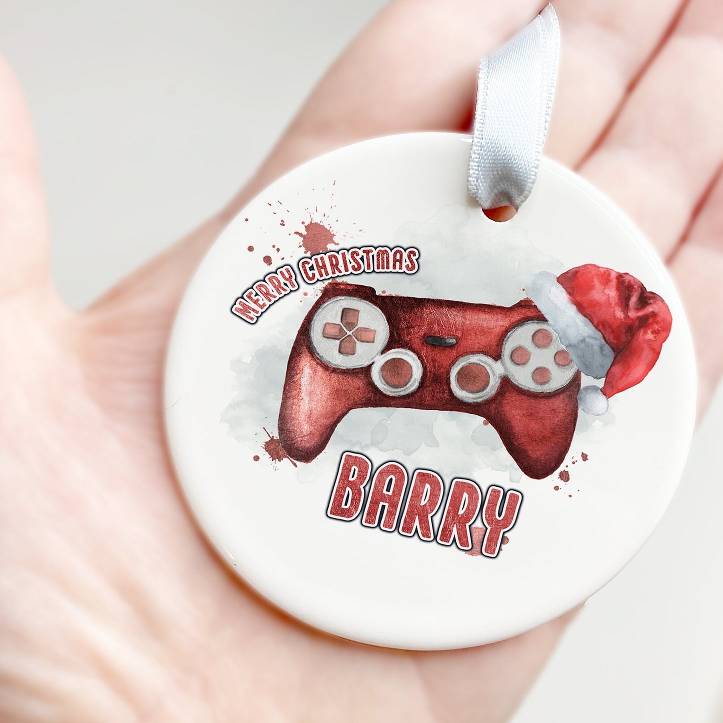 White Ceramic personalised Christmas bauble in gift box. Festive Red coloured gaming Controller with christmas hat and matching red text in the words Merry Christmas Name.