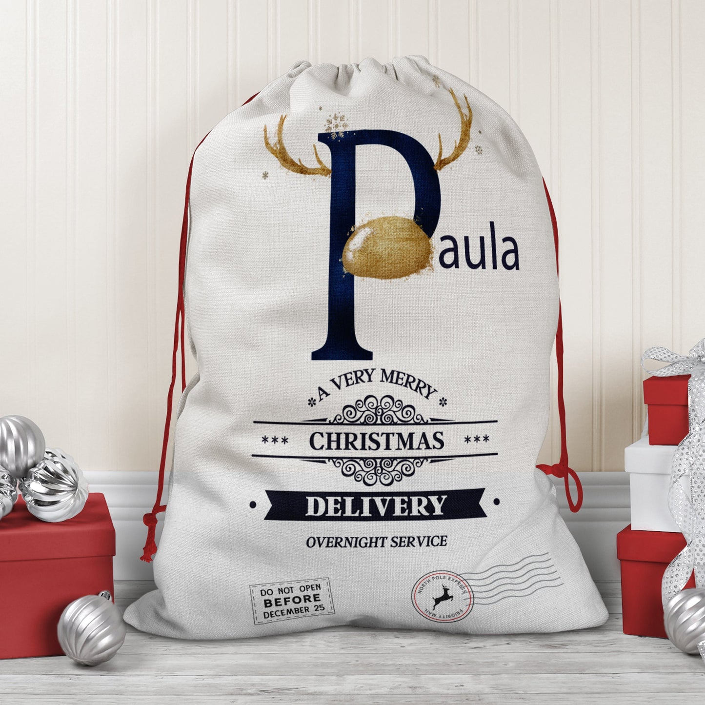 Large natural looking Linen Sack with printed Reindeer antler and Navy Initial letter with gold coloured nose & text Name is written in Navy above the words A very merry Christmas Delivery Overnight service and two North pole style delivery stamps