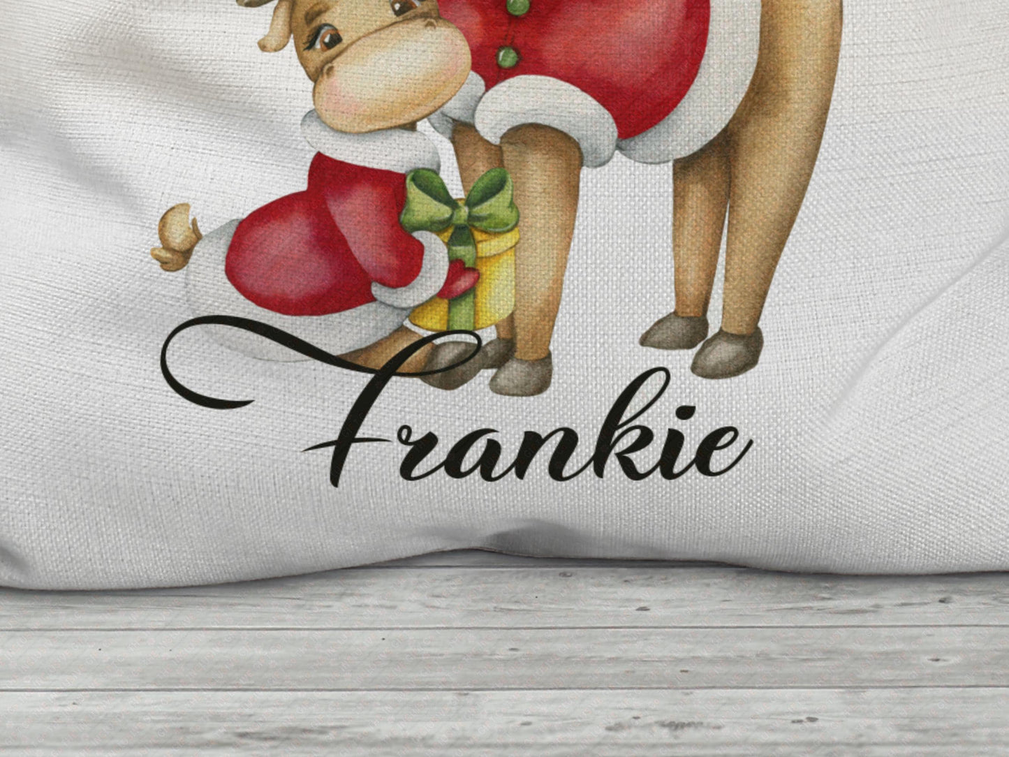 Close-up of the bottom of  a personalised Christmas Santa sack showing the  a small reindeer in a red coat holding a yellow gift with a green ribbon. The name "Frankie" is printed in elegant black script beneath the illustration on an off white - beige Linen fabric with visible texture.