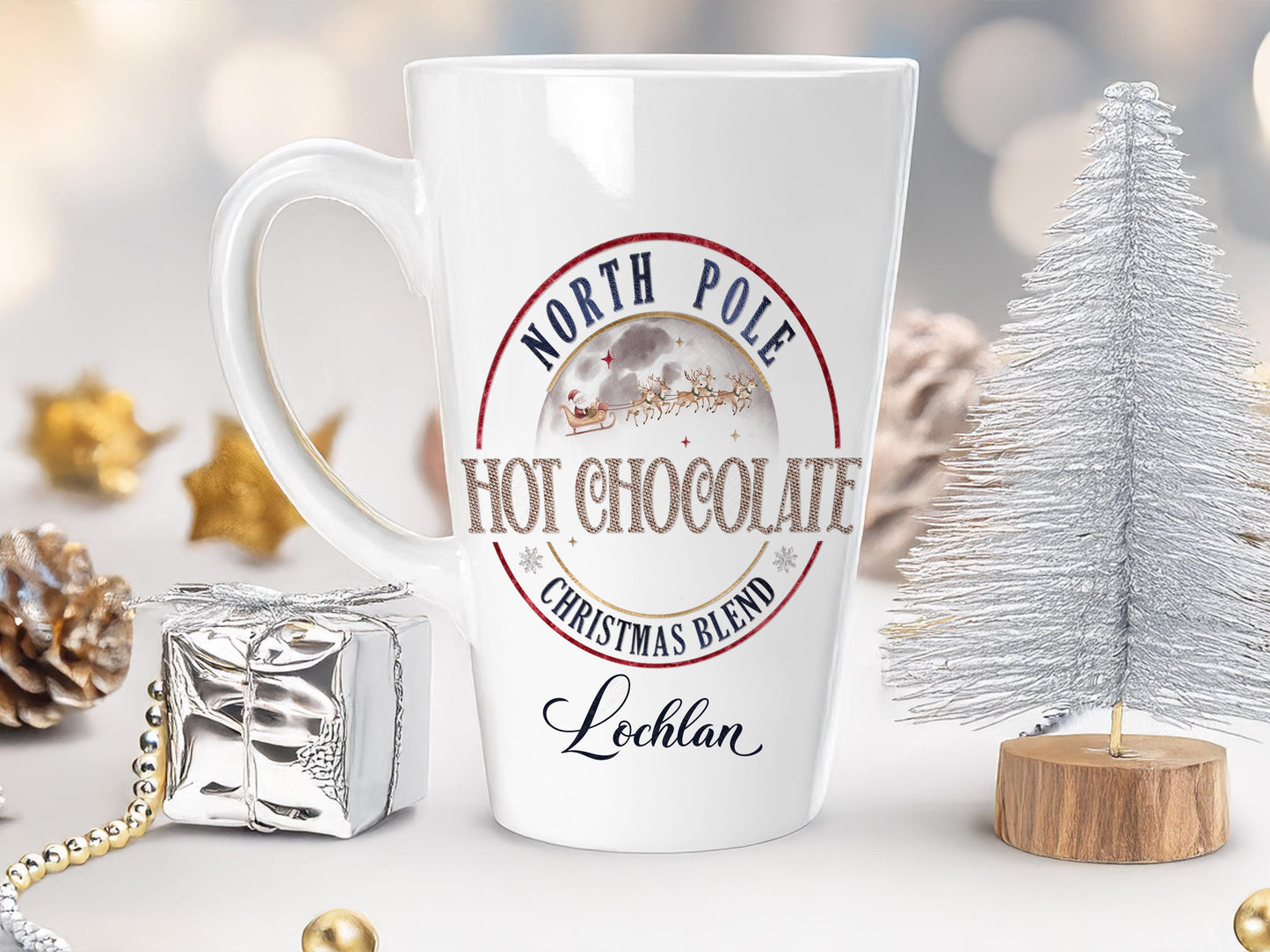 Large tapered Latte style White ceramic mug with "North Pole Hot Chocolate Christmas Blend" design and the name Lochlan printed at the bottom any name can be printed. A Wintery moon sits above the words Hot Chocolate with santa and his sleigh being pulled by a team of reindeer throough the sky.