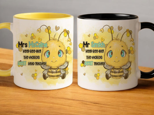 Two Ceramic mugs sitting on an oak table one with a glossy yellow handle and rim and one with a glossy black handle and rim. A cute cartoon style bee with bright blue eyes is printed on each side of the mug with the words Teacher name Keep beeing the BEST Teacher in black and matching blue