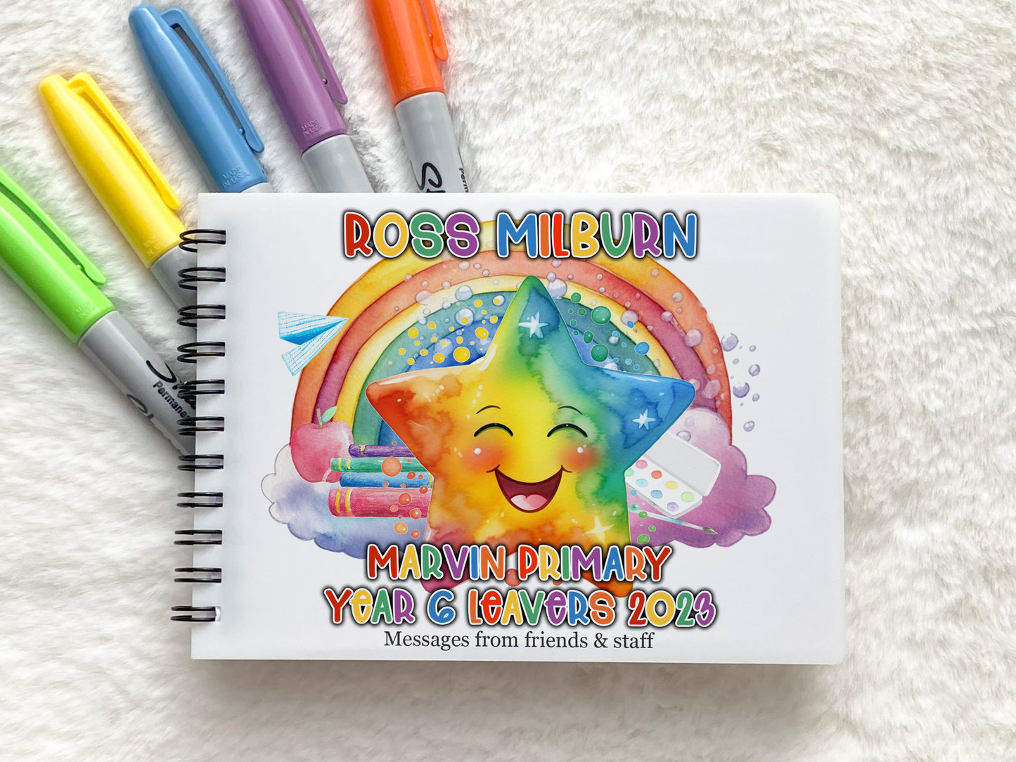 A6 Spiral bound notebook with plastic cover. Rainbow coloured design featuring happy smiling star, books, a rainbow and paper aeroplane. matching rainbow coloured Text reads, Name School name Yea 6 Leavers 2023 messages from friends and staff