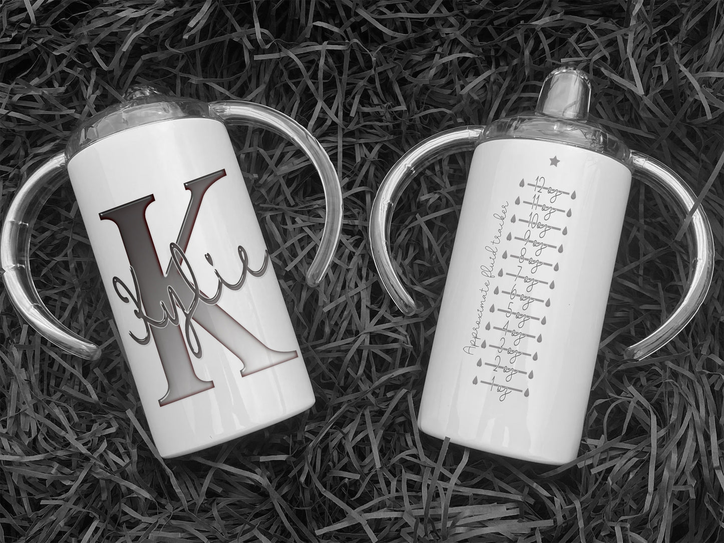 White Stainless steel Sippy cup with clear plastic lid with spout and large handles. A glossy Grey and white Initial with Name in script written across in matching grey. the back has an approximate fluid guide in matching grey