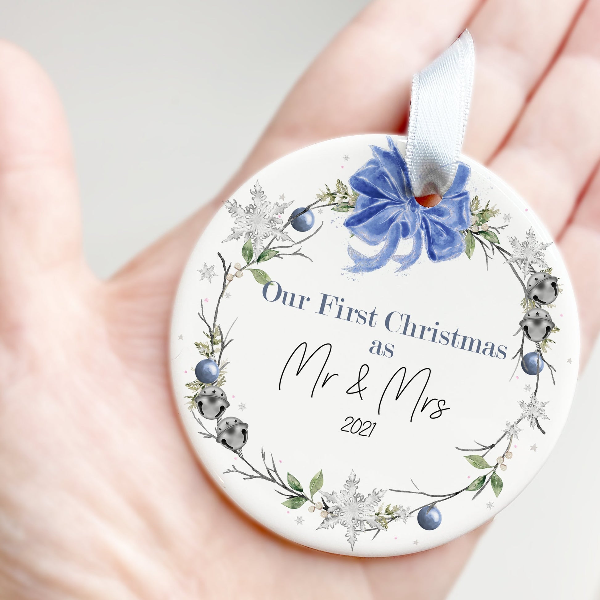 Flat Ceramic white bauble printed with Blue and green floral wreath & sleigh bells topped with a blue bow design Message reads Our First Christmas as Mr & Mrs (year)