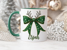 Load image into Gallery viewer, White Ceramic mug with a Green rim and handle printed with a Festive RGreen &amp; Gold bow. Topped with Glittery Reindeer Antlers with matching Name. Personalised with any name and printed on both sides. Bows also available in Red, Dark blue, Light Blue and Pink
