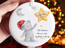 Load image into Gallery viewer, Bright white flat circle ceramic ornament with white satin ribbon. Printed with a gentle comforting remberance design featuring a soft grey bear wearing a santa hat and clutching a gold star standing under a greay crescent moon pointing up to a bright yellow Gold shining star featuring baby or childs name and relevant dates. Black text sits below the star that reads &quot;This Christmas theres an extra bright star in the sky.&quot;
