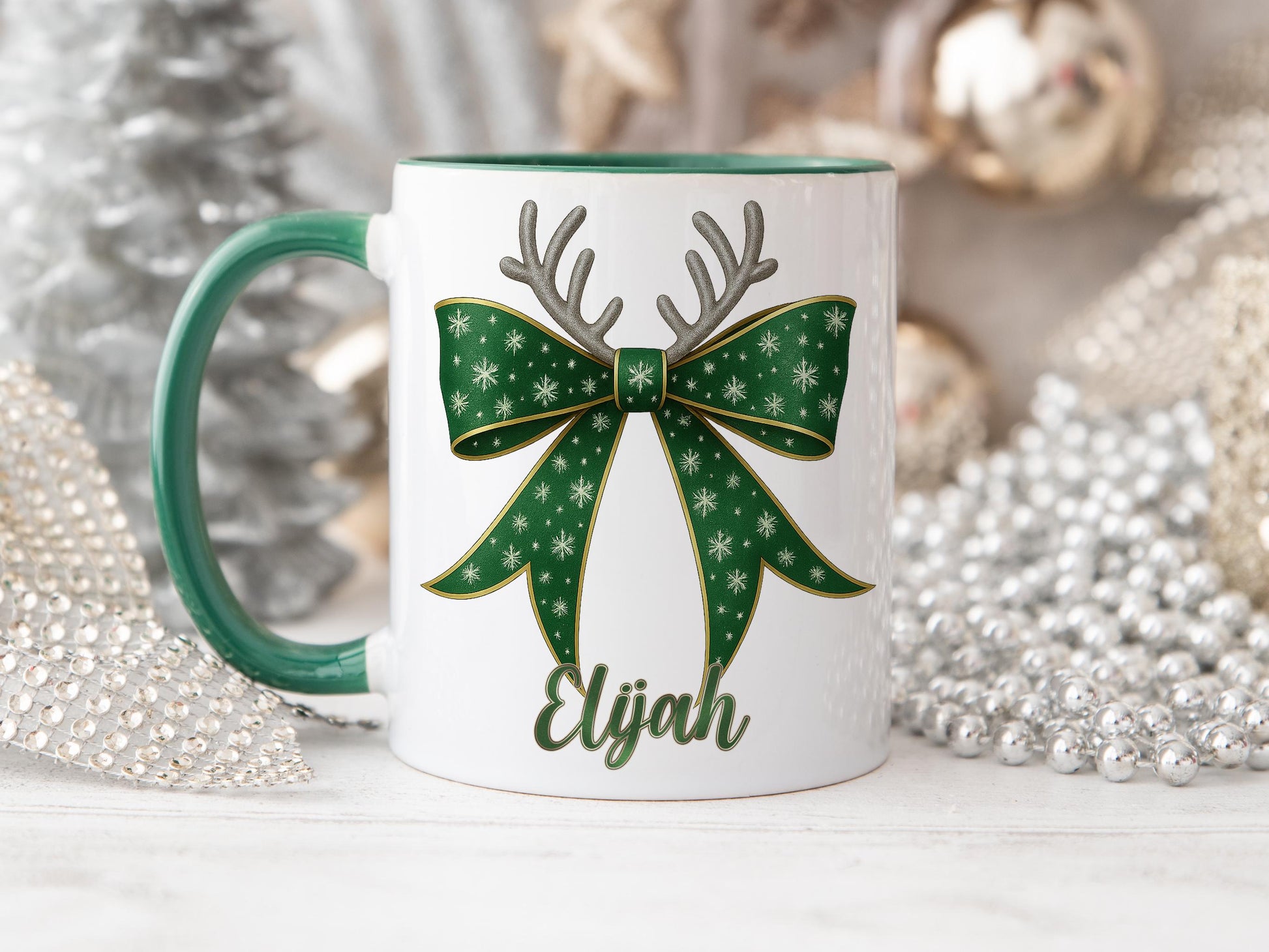 White Ceramic mug with a Green rim and handle printed with a Festive RGreen & Gold bow. Topped with Glittery Reindeer Antlers with matching Name. Personalised with any name and printed on both sides. Bows also available in Red, Dark blue, Light Blue and Pink