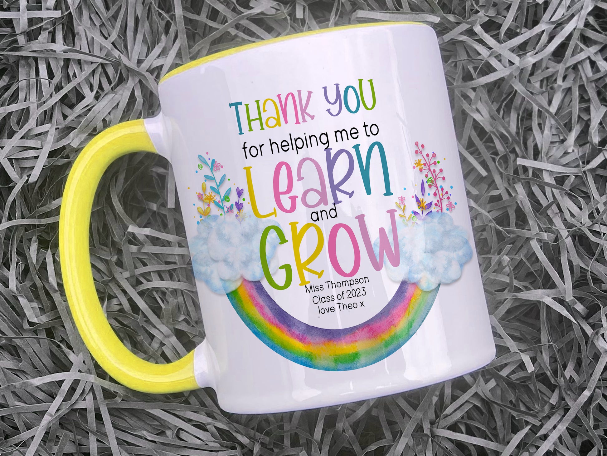 Ceramic mug with yellow handle and rim. An upside down rainbow with clouds and matching florals at either end with the words Thank you helping me to Learn and Grow. Teachers name Class of 2023 and optional from name