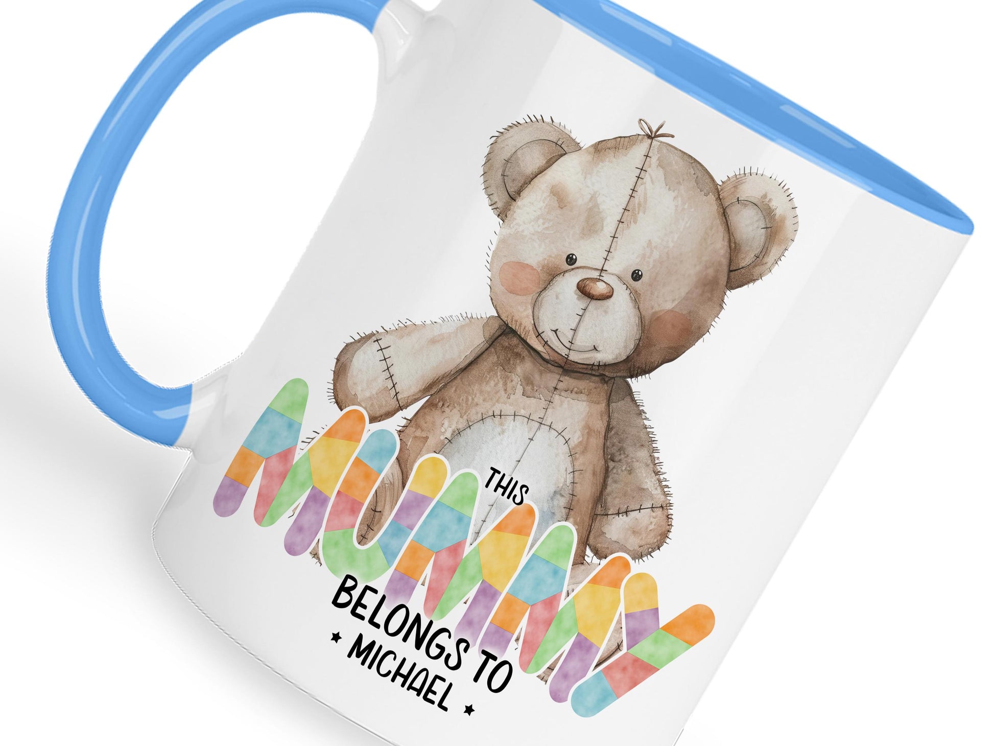White ceramic mug with glossy Blue handle, rim and inner. Design shows A cute brown patchwork teddy bear and This Mum belongs too Names in coloured patchwork.

Personalised with as many names as you need