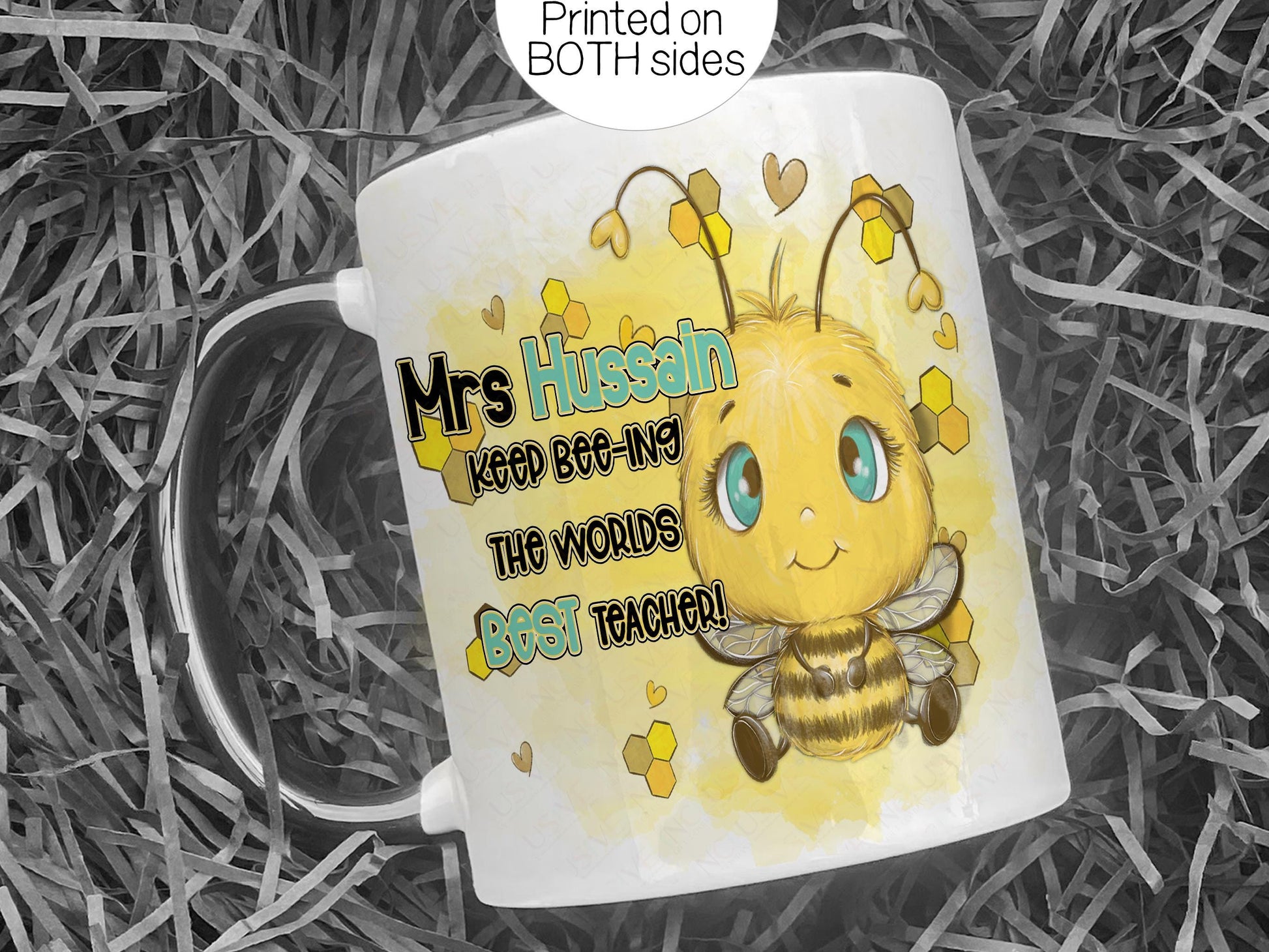 white glossy mug with black handle and rim laying on a bed of black shredded paper. A cute cartoon style bee with bright blue eyes is printed on each side of the mug with the words Teacher name Keep beeing the BEST Teacher in black and matching blue. Mugs are printed on both sides