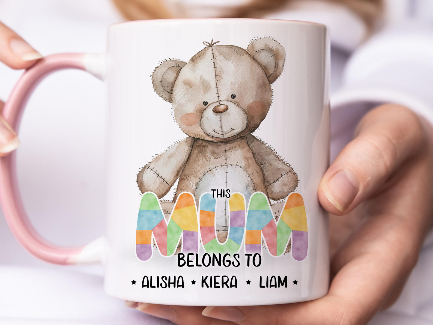 White ceramic mug with glossy pink handle, rim and inner. Design shows A cute brown patchwork teddy bear and This Mum belongs too Names in coloured patchwork.

Personalised with as many names as you need