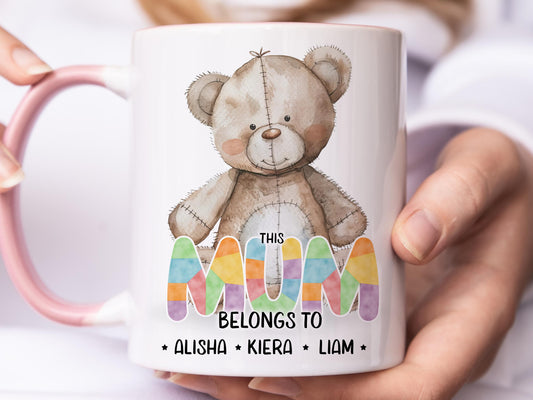 White ceramic mug with glossy pink handle, rim and inner. Design shows A cute brown patchwork teddy bear and This Mum belongs too Names in coloured patchwork.

Personalised with as many names as you need
