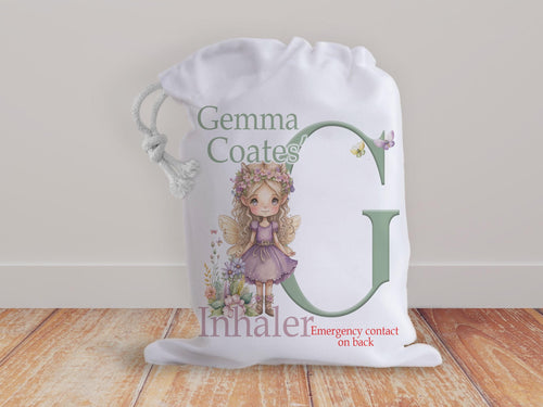 White drawstring bag with a beautiful fairy and initial letter in muted natural colours. Bag shows Initial of first name and a character with text reading name inhaler if you choose to have emergency contact or instructions on back it will state this is available on the front.