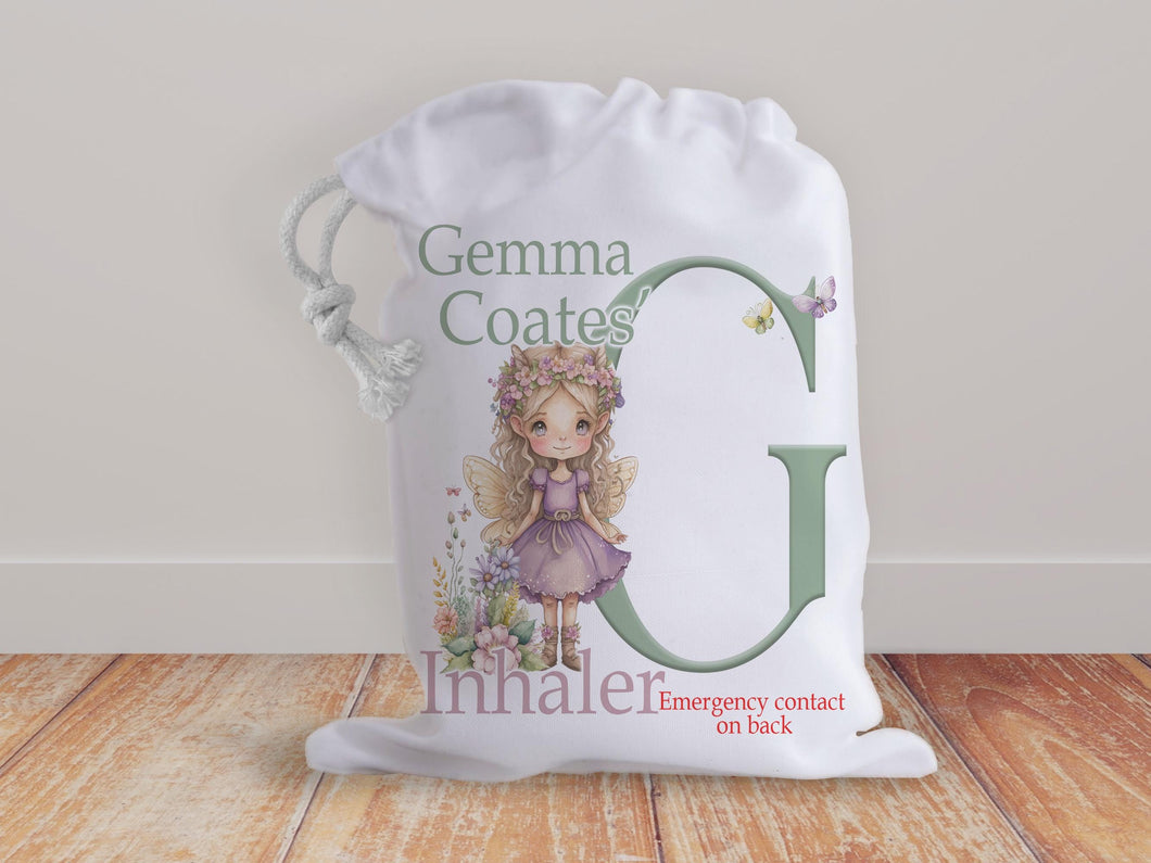 White drawstring bag with a beautiful fairy and initial letter in muted natural colours. Bag shows Initial of first name and a character with text reading name inhaler if you choose to have emergency contact or instructions on back it will state this is available on the front.