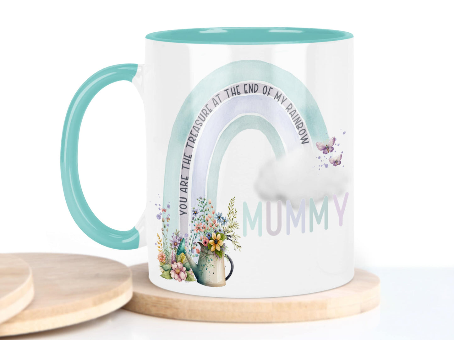 White ceramic mug with glossy mint green handle, rim and inner. Design shows A Mint green and grey coloured rainbow with flowers and watering can at one end, cloud & butterflys at the other.