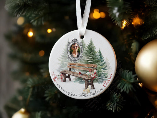 Printed Memorial Christmas ornament with framed photo of your loved one, against a festive winter background of pine trees, rustic wooden bench, a Robin and Roses, A personalised remembrance quote reading ‘Name, memories of you shine brighter at Christmas.’