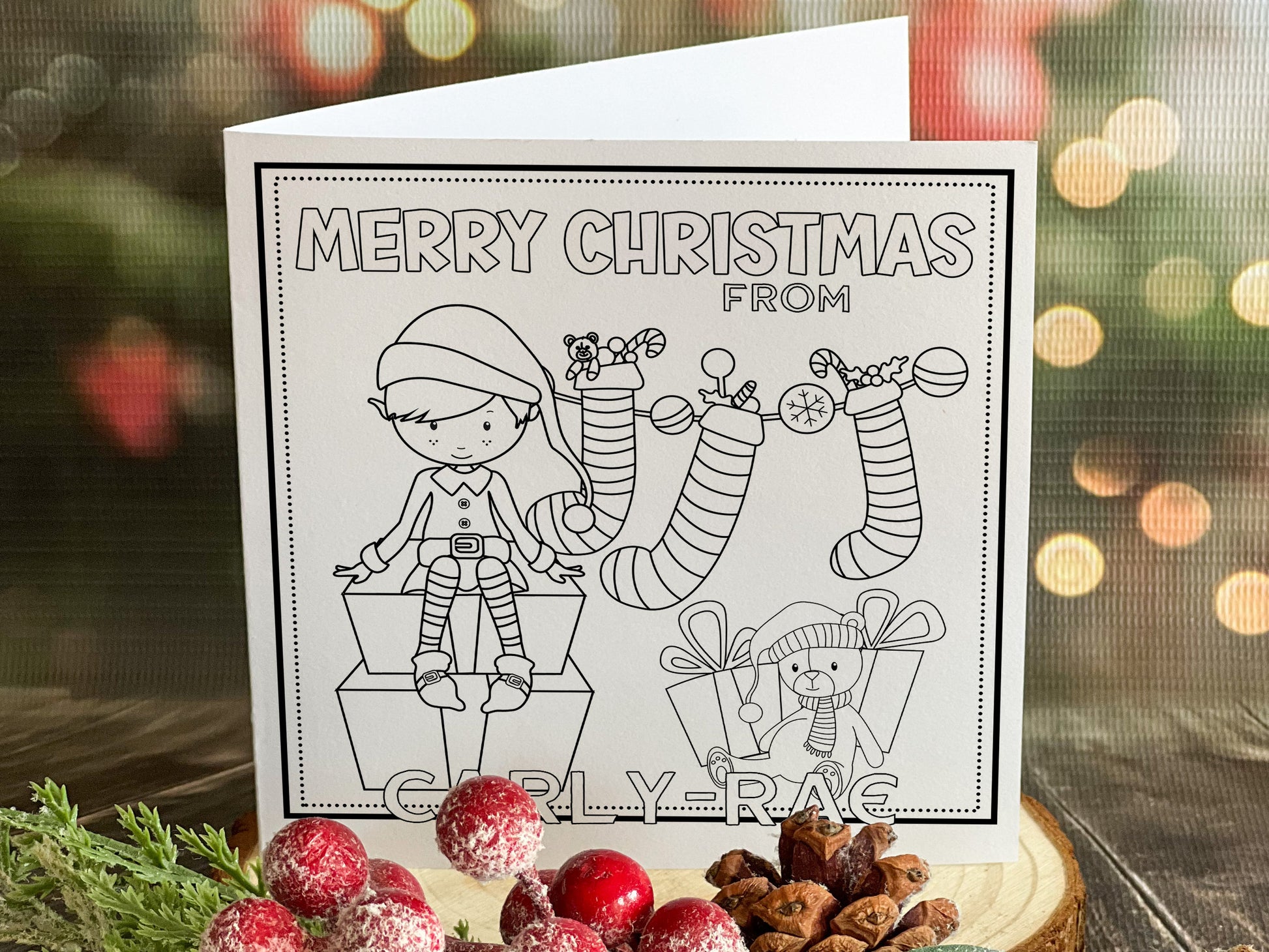 Colour your own White 5x5 inch sq card with black and white line drawing of Cute festive Elf with teddy stockings and gifts  . Wordings reads Merry Christmas from Name)