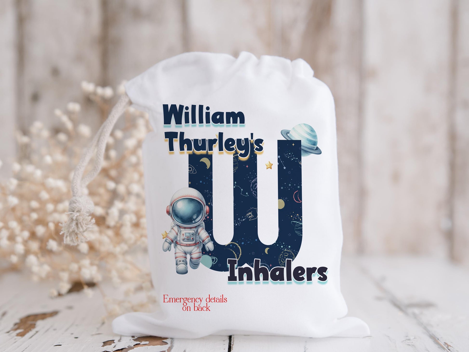 White drawstring bag. Printed with Initial of first name in a space theme with astronaut & text reading name's inhaler if you choose to have emergency contact on back it will state this is available on the front.