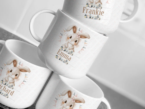 Image shows a stack of 4 white childrens polymer plastic mugs (teacup sized) All have a cute Easter bunny with eggs design. Comes with or without the bunny wearing a cute pink gingham bow.