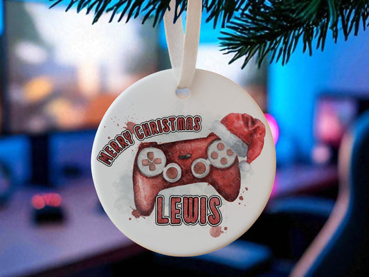 Personalised flat white ceramic Christmas bauble featuring a Christmas gamer themed design -  game console controller in a choice of 6 colours - Red, Blue, Gold, Purple with flowers, Teal with Flowers, Pink with flowers The words Merry Christmas and name or gamertag coloured to match the controller – a perfect stocking stuffer, Gaming room decoration or gift for dad