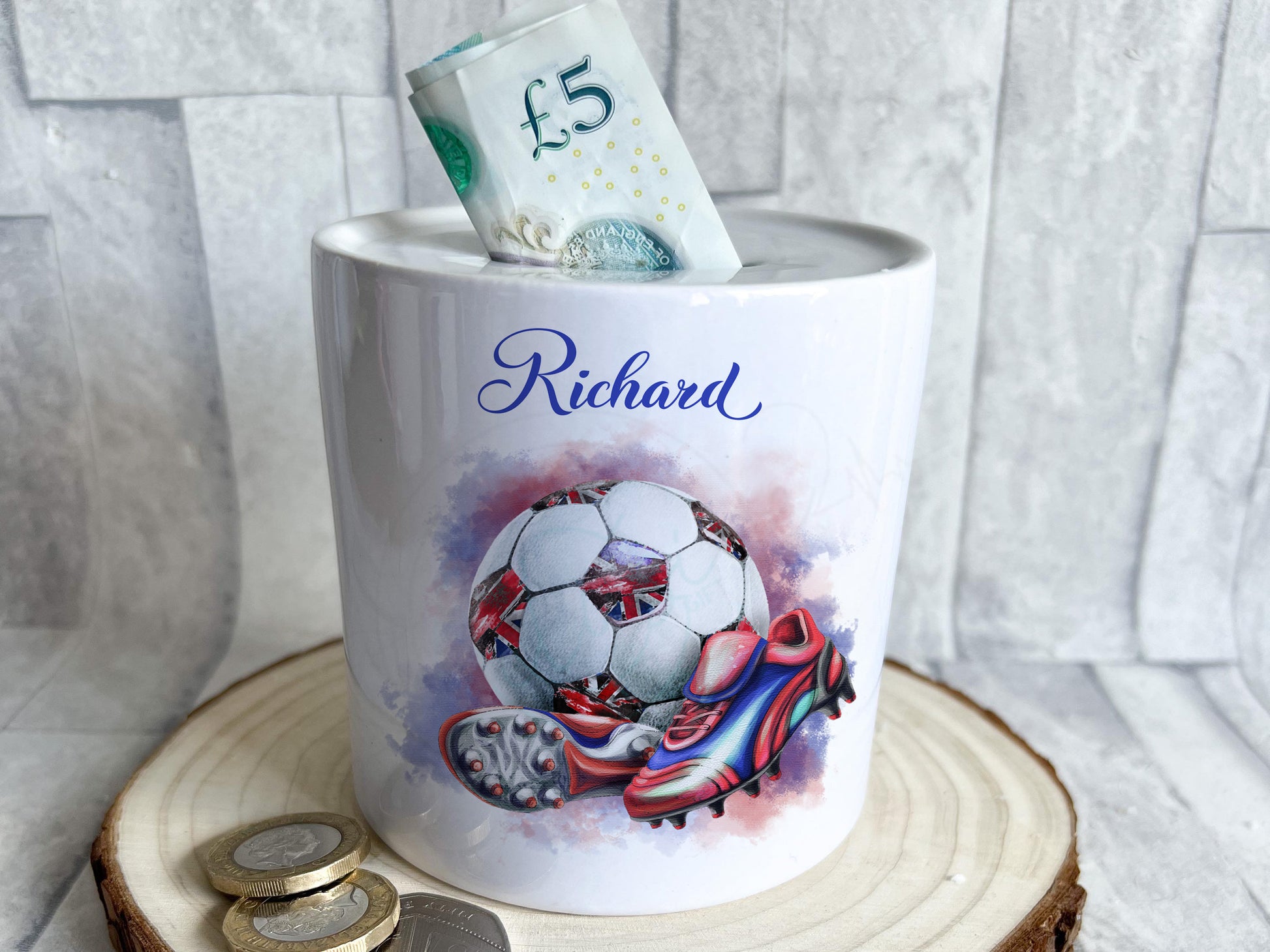 Bright white round ceramic money box with red white and blue coloured football with union jack patches and red and blue boots. Personalised with any name in matching blue text.