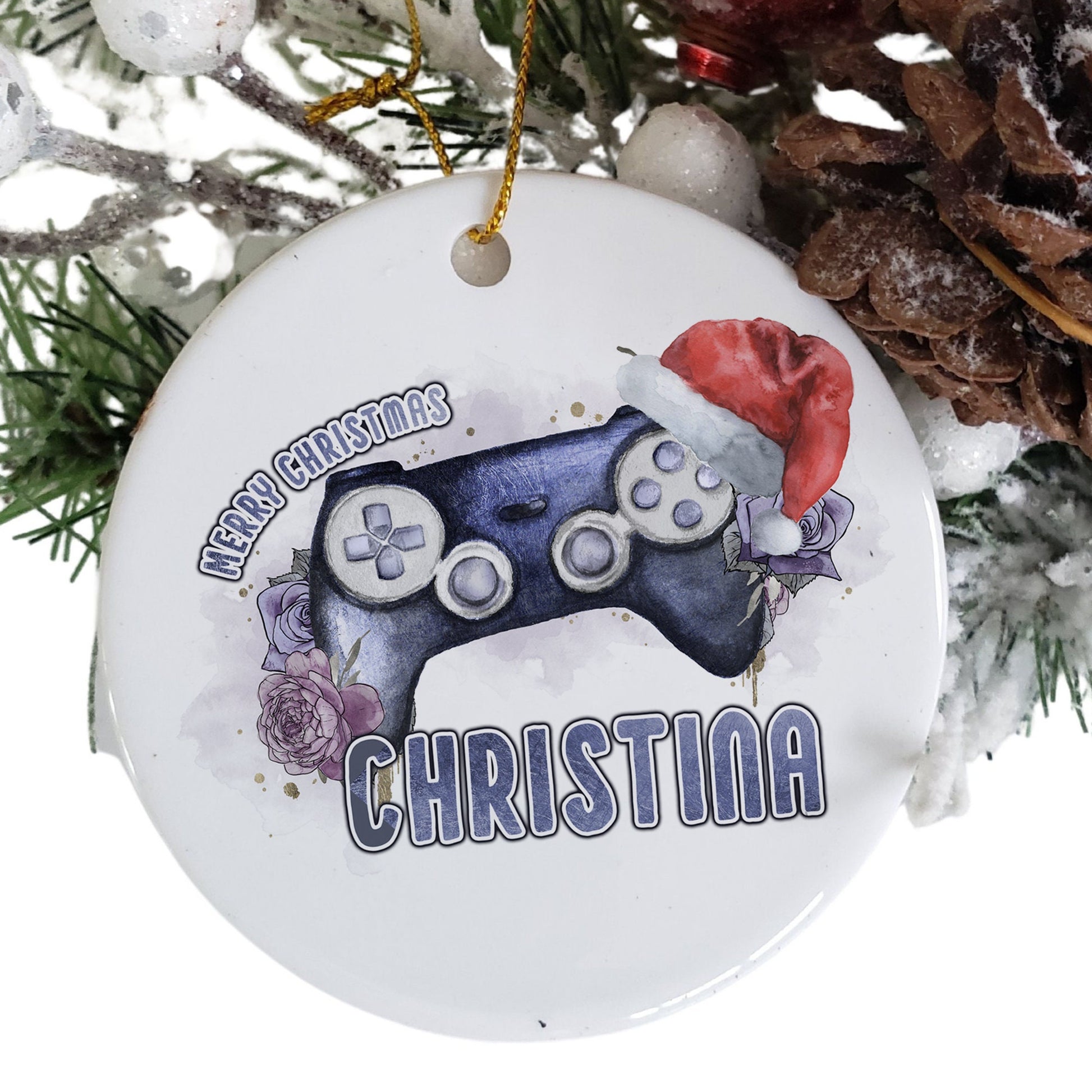 White Ceramic personalised Christmas bauble in gift box. Festive Purple coloured gaming Controller with purple florals and christmas hat and matching purple text in the words Merry Christmas Name.