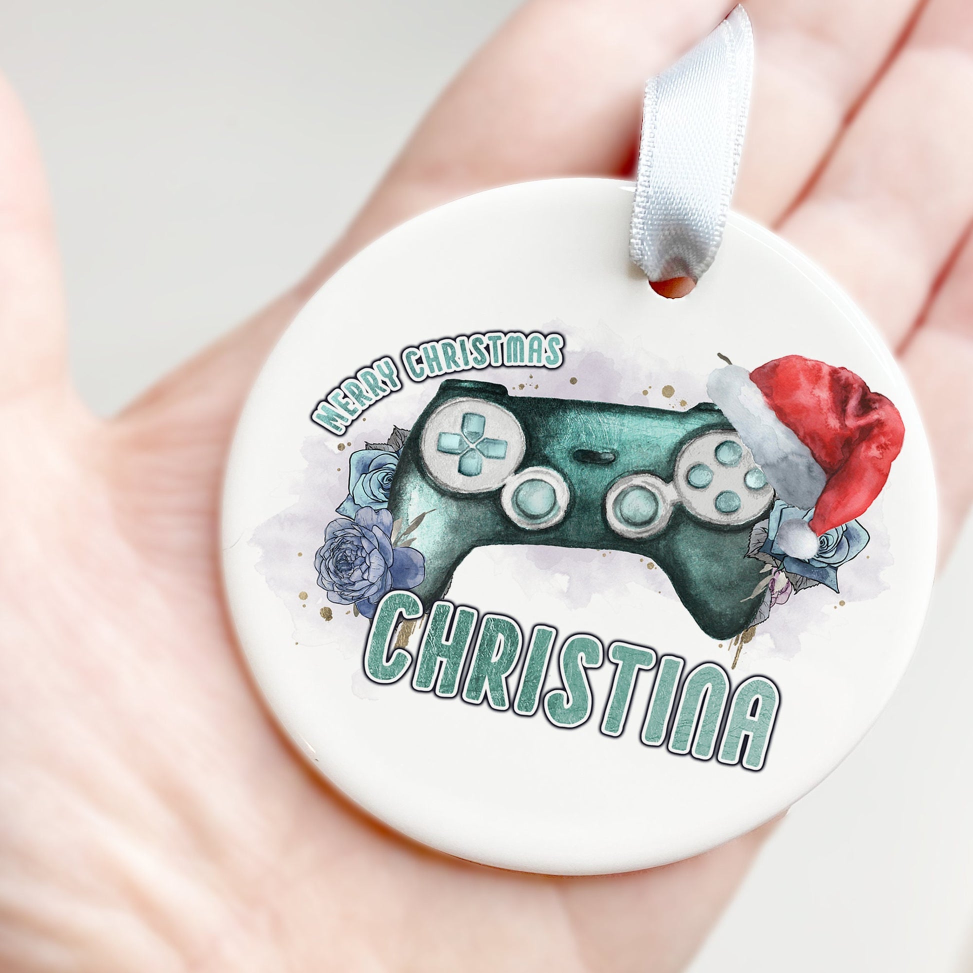 White Ceramic personalised Christmas bauble in gift box. Festive teal coloured gaming Controller with teal florals and christmas hat and matching teal text in the words Merry Christmas Name.