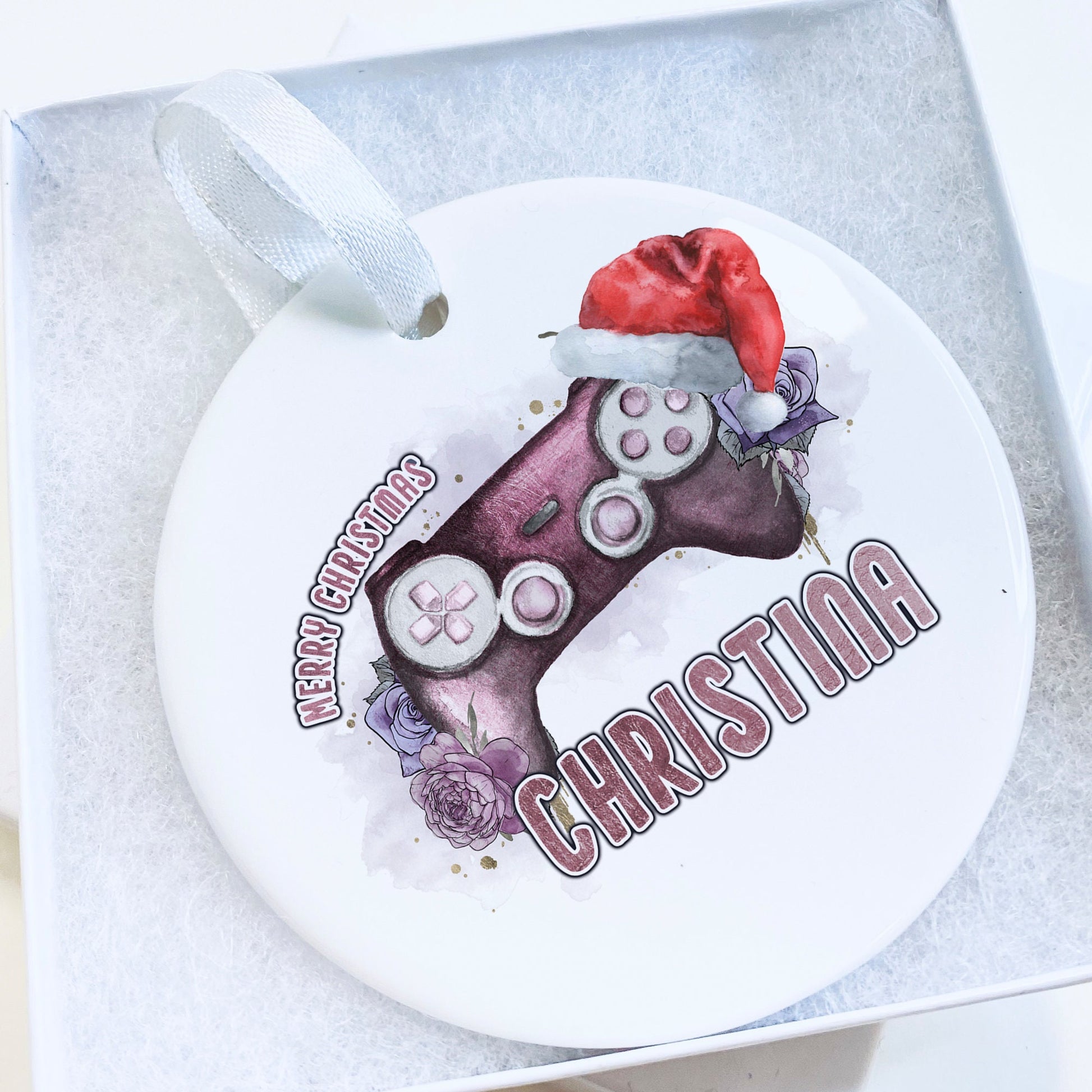 White Ceramic personalised Christmas bauble in gift box. Festive Pink coloured gaming Controller with pink florals and christmas hat and matching pink text in the words Merry Christmas Name.