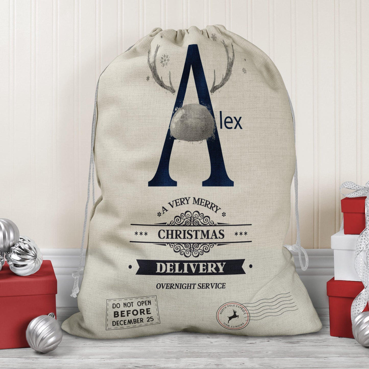 Large natural looking Linen Sack with printed Reindeer antler and Navy Initial letter with silver coloured nose & text Name is written in navy above the words A very merry Christmas Delivery Overnight service and two North pole style delivery stamps