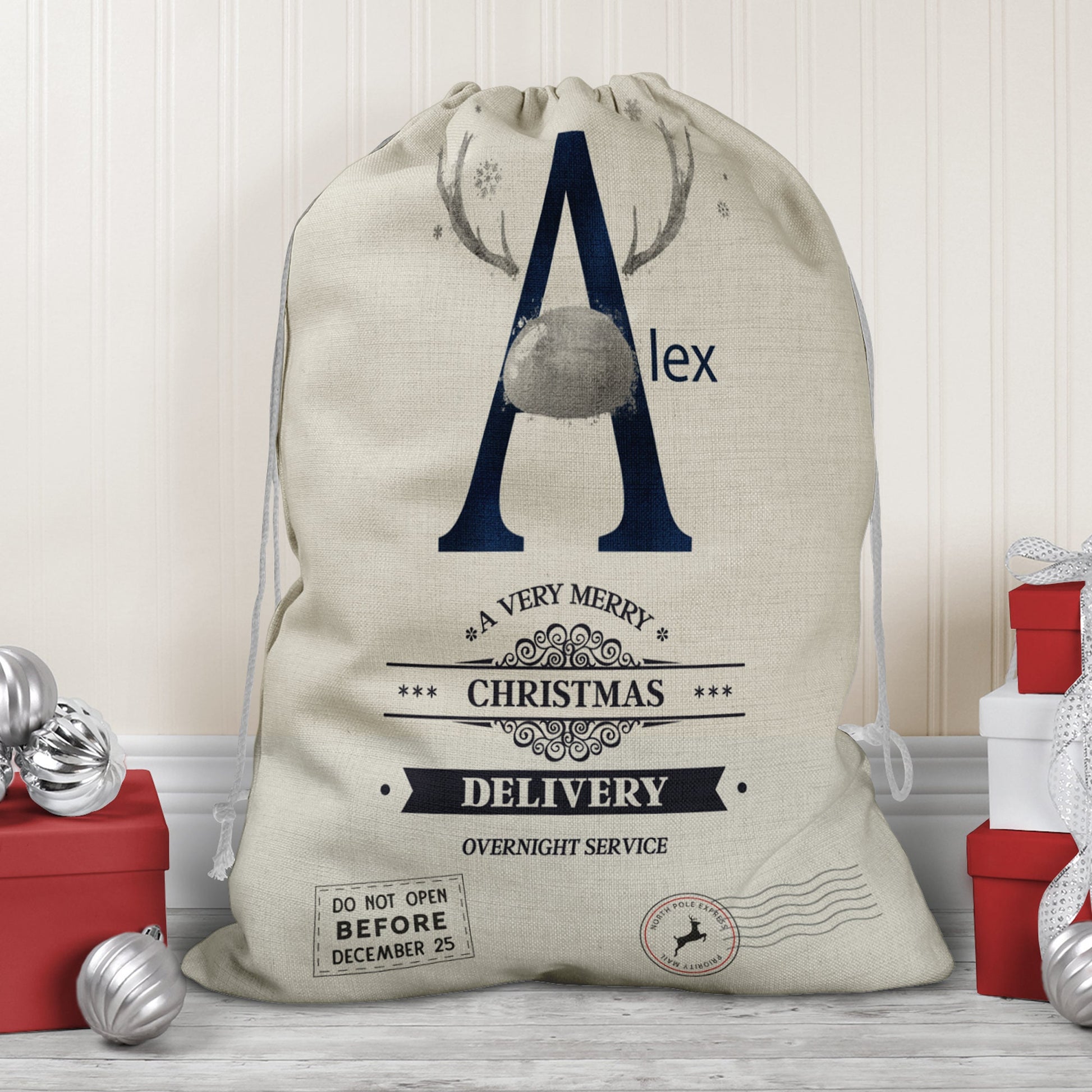 Large natural looking Linen Sack with printed Reindeer antler and Navy Initial letter with silver coloured nose & text Name is written in navy above the words A very merry Christmas Delivery Overnight service and two North pole style delivery stamps