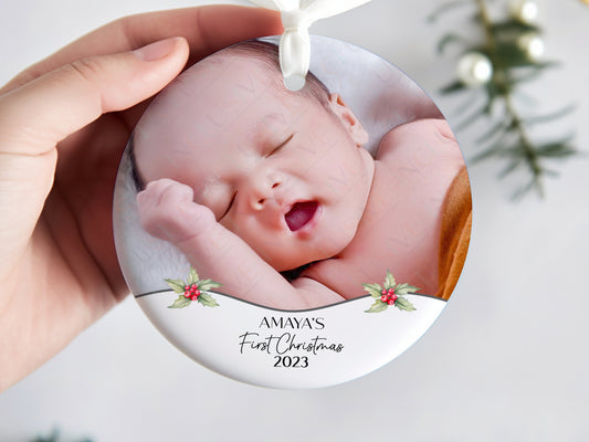 7cm round ceramic bauble with photo of your choice framed with holly and the text Name&#39;s First Christmas 2023 in black. Perfect for baby on their own or photos of baby with mum dad or other family members