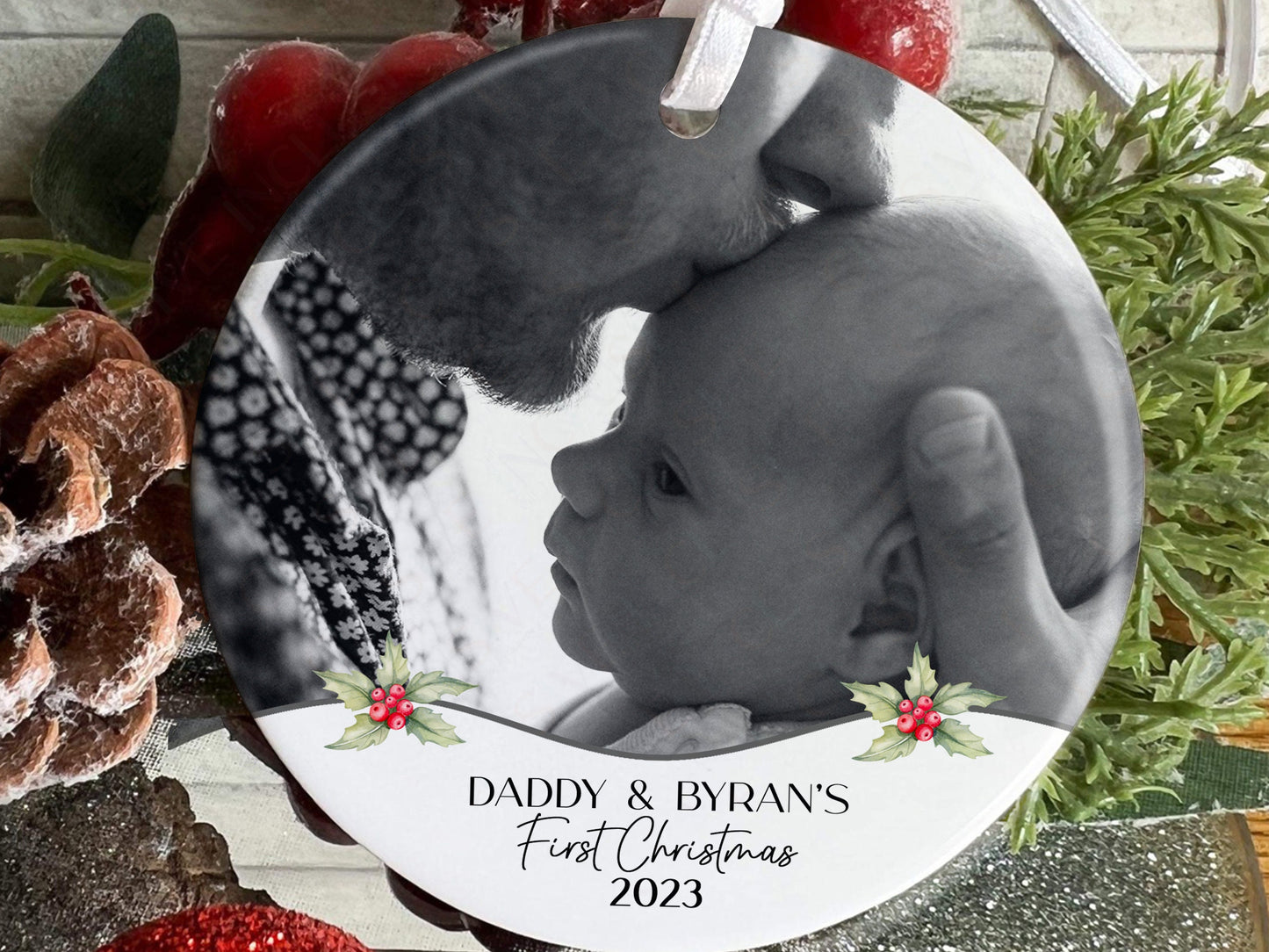 7cm round ceramic bauble with photo of your choice framed with holly and the text Name&#39;s First Christmas 2023 in black. Perfect for baby on their own or photos of baby with mum dad or other family members