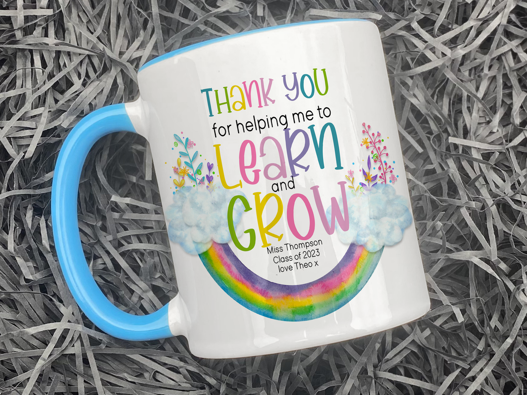 Ceramic mug with blue handle and rim. An upside down rainbow with clouds and matching florals at either end with the words Thank you helping me to Learn and Grow. Teachers name Class of 2023 and optional from name