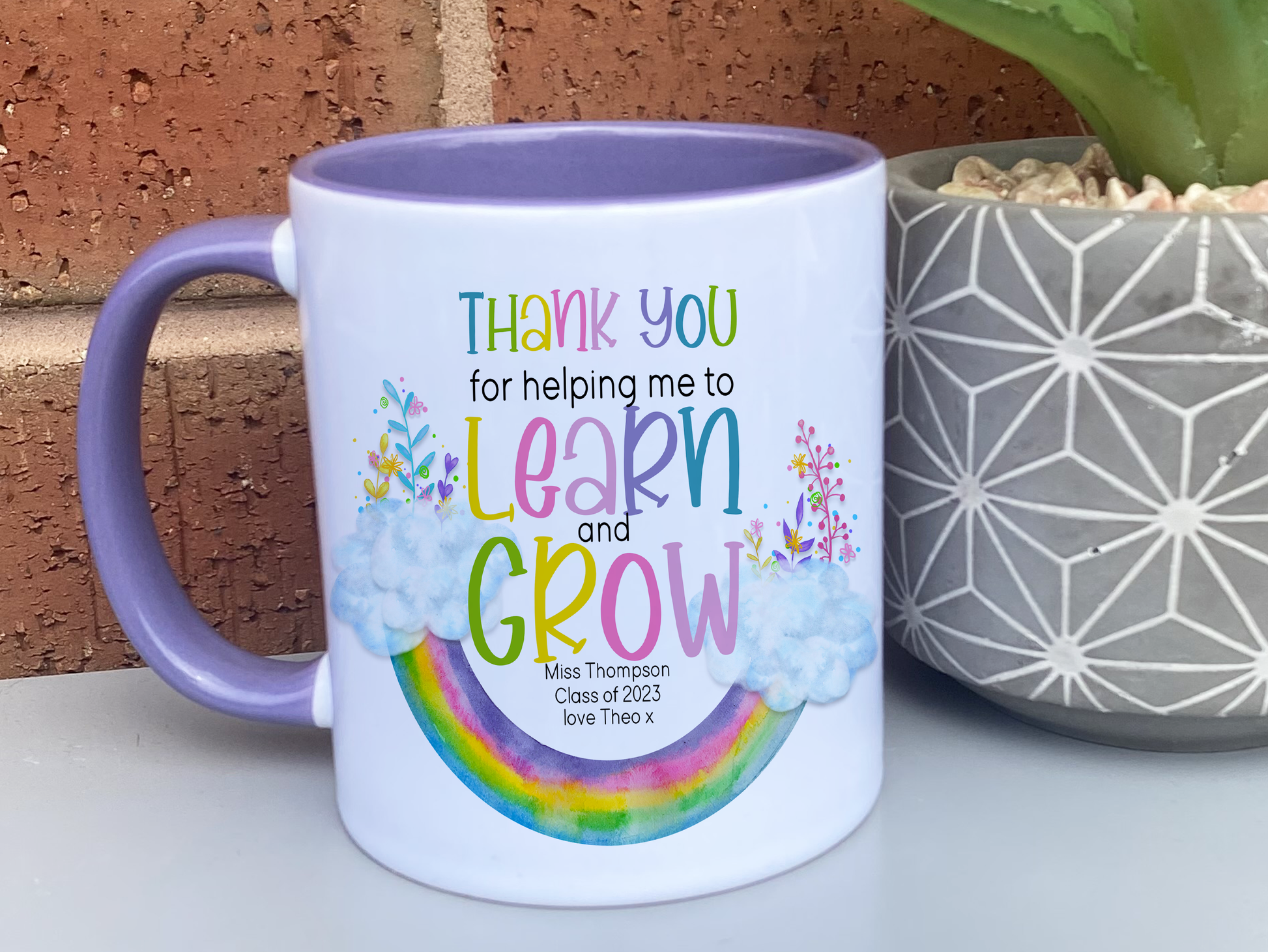 Ceramic mug with purple handle and rim. An upside down rainbow with clouds and matching florals at either end with the words Thank you helping me to Learn and Grow. Teachers name Class of 2023 and optional from name