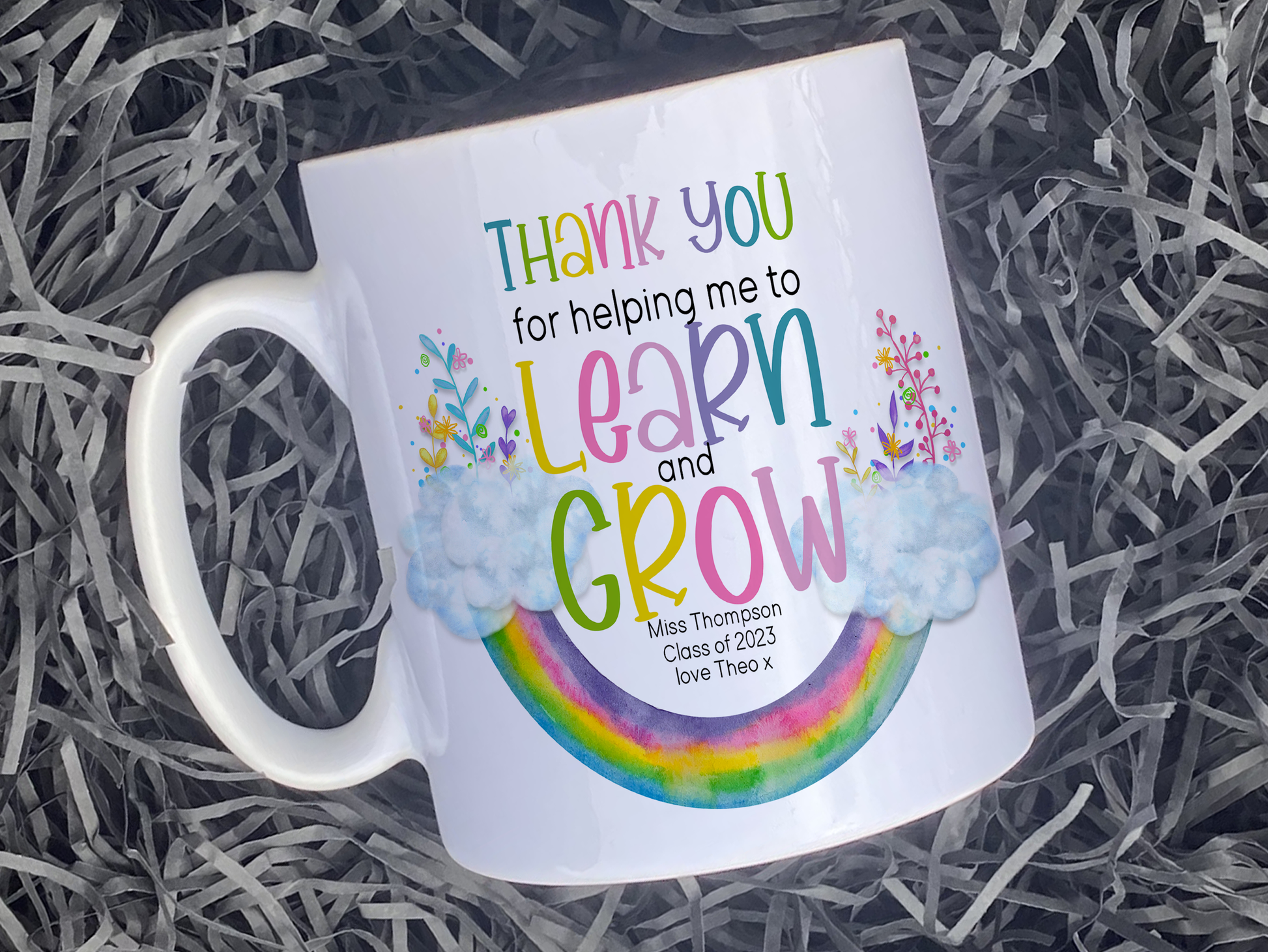 Plain white Ceramic mug. An upside down rainbow with clouds and matching florals at either end with the words Thank you helping me to Learn and Grow. Teachers name Class of 2023 and optional from name