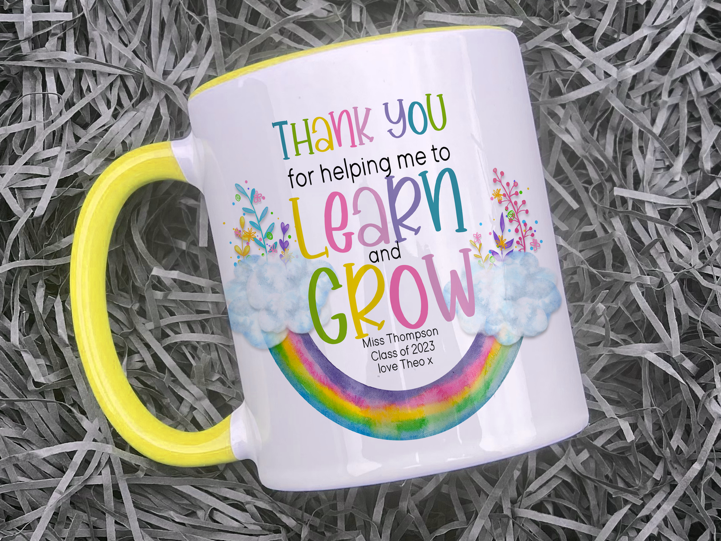 Ceramic mug with yellow handle and rim. An upside down rainbow with clouds and matching florals at either end with the words Thank you helping me to Learn and Grow. Teachers name Class of 2023 and optional from name