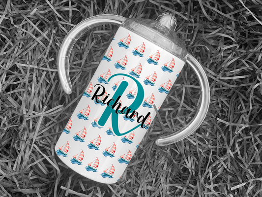 White Adult sippy cup with sailing boat design and inital and name, adaptive cup with Spouted lid for adults with disabilities. Image shows a single cup on black background showing sailing boat pattern and Large Initial with name across the middle. 